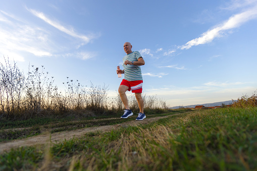 A fit senior man takes a refreshing evening run in the great outdoors, bathed in the warm hues of the setting sun.