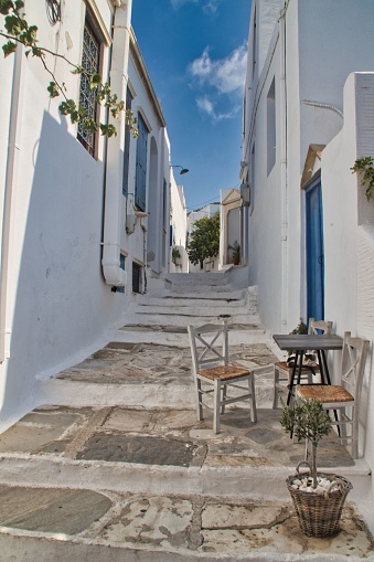 A vibrant, narrow alleyway with two chairs with table illuminated by bright sunlight