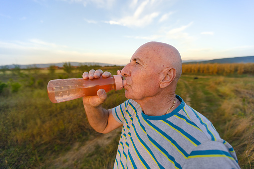 An elderly man enjoys the pure simplicity of water, savoring each drop after a walk in the natural world.