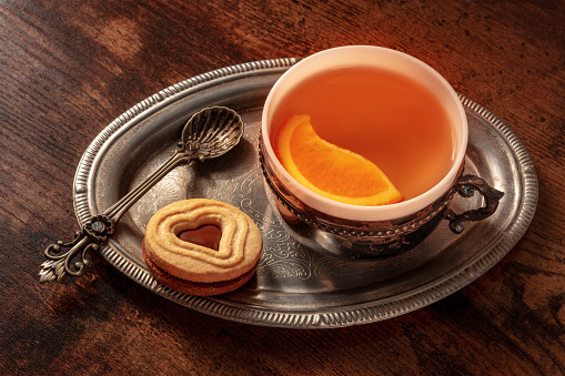 Orange tea with cookies, a cup on a vintage tray on a dark rustic wooden background