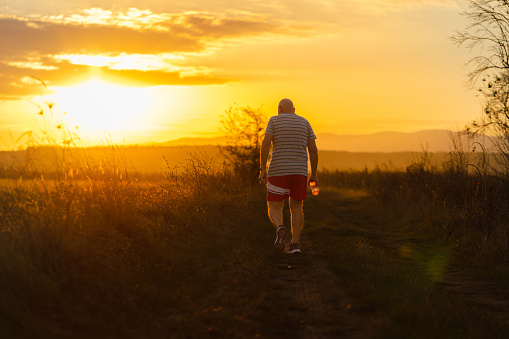 A senior man embraces the beauty of a peaceful evening run amidst the serenity of nature in the golden hour.