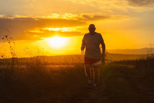 A senior man embraces the beauty of a peaceful evening run amidst the serenity of nature in the golden hour.