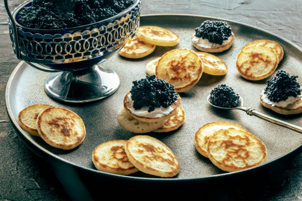 istock Blinis with black caviar, on a festive dish on a black background, mini pancakes 1738798243