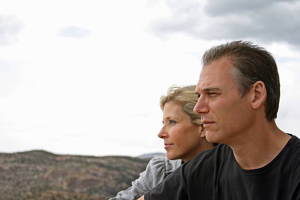 Couple look out across the landscape Mature, middle-aged married couple taking a thoughtful break in their hiking. They're staring off into the distance with white copy space in front of them. 40 49 years stock pictures, royalty-free photos & images
