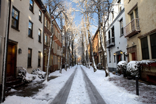 A tiny street lined with old row houses on a sunny snow covered morning.