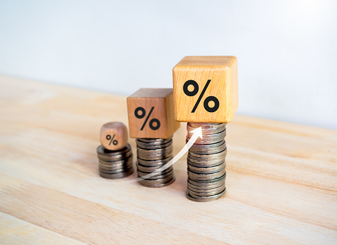 Rising arrow on wooden cube blocks with percentage icon on coin stacked bar graph chart steps on white background. Investment, profit percent, income, business growth, economic improvement concepts.
