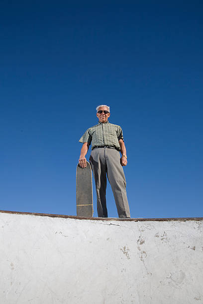 A senior man stands at the edge of a skate park bowl. Loads of copy space.