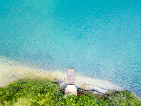 Aerial view of beautiful wooden pier, sea or lake bay, sandy beach at sunset in summer. Top view of jetty, transparent blue water with waves. Tropical landscape at a Vacation destination. High quality photo