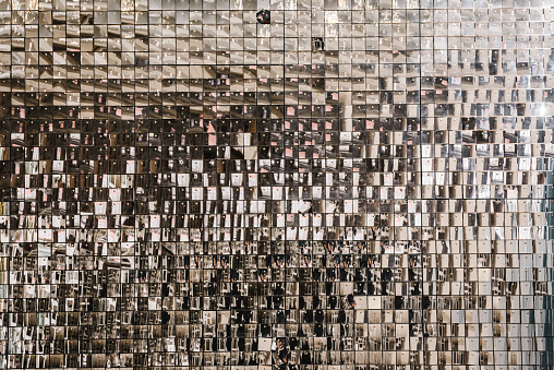 Silver glitter sparkles on background. Space with flickering and glittering metallic particles. Wall is made of square glittering sequins. Decor and interior decoration. Place for text. Closeup.