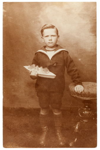 Vintage sepia toned portrait of a young boy wearing a sailor's outfit holding a toy boat. Some dust and scratches which convey age of original image. Circa 1910.