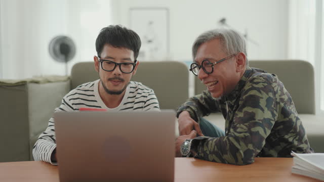 Asian Freelancer and Senior Father Working on Laptop in Cozy Living Room.