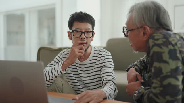 Multigenerational Bonding: Asian Man Working from Home, Sharing a Smile and Conversation with His Senior Father.