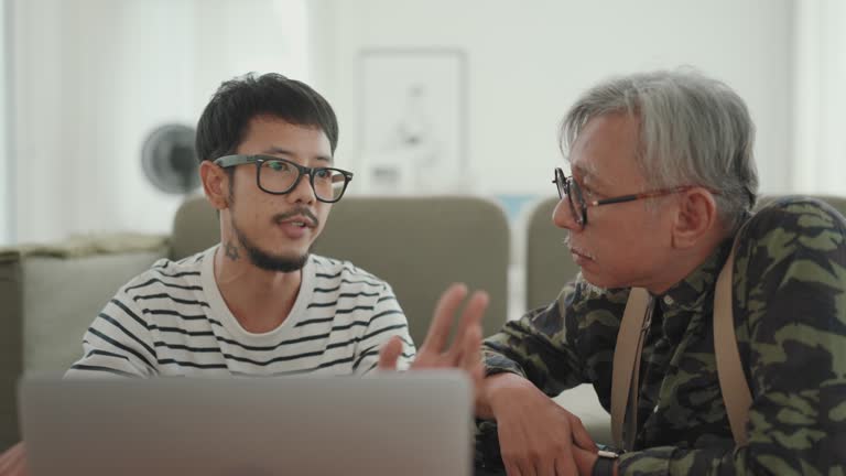 Multigenerational Bonding: Asian Man Working from Home, Sharing a Smile and Conversation with His Senior Father.