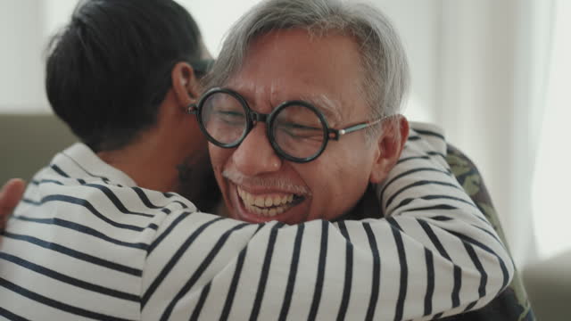 Asian Man Freelancer Embracing with His Father: Heartwarming Moments of Togetherness and Connection in Home Office..