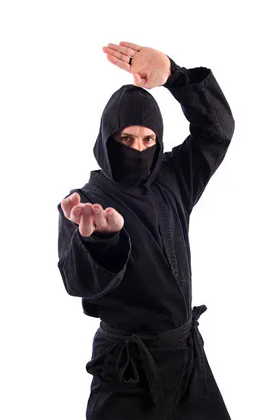 This color photo shows a martial arts ninja in black simultaneously executing a knife-hand strike with one hand and a knife-hand upper block with the other. The ninja warrior is visible from mid-thigh to the top of his head. The image is isolated on a white background.