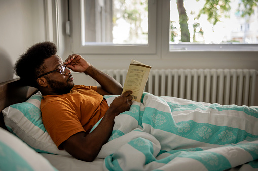 Young man reads a book in bedroom in the morning
