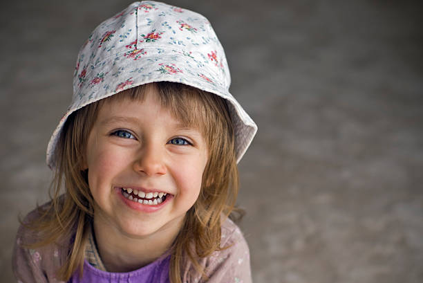 She wears a straw hat and she jokingly smiles with her mouth and eyes.