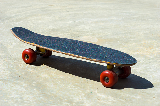 Side top view of penny board with red wheels stands on the ground in a skatepark.