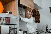 Rear View Of Cute Female Putting Clean Mugs In Cupboard