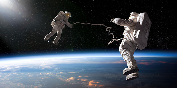 Two astronauts in full spacesuits with backpacks on a space walk with tethers, facing each other with hands out. The astronauts are in front of planet earth and some distant stars are also visible.
Earth image from NASA: https://eoimages.gsfc.nasa.gov/images/imagerecords/50000/50205/ISS027-E-012224_lrg.jpg