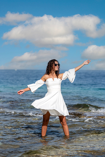 Happy woman wearing white dress poses in the sea