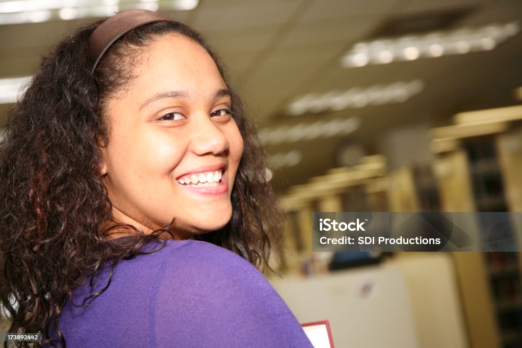 Sorridente studente di College tornitura posteriore nella Libreria - Foto stock royalty-free di 18-19 anni