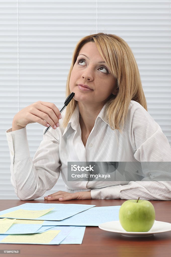 Young Woman Working And Thinking Young woman working and thinking with sitting at the table. Papers and green apple on the table. Adult Stock Photo