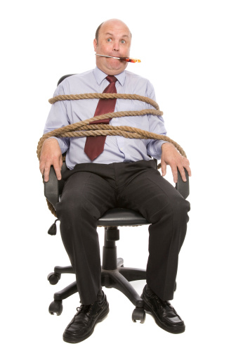 A business man tied up with rope and scissors in mouth.