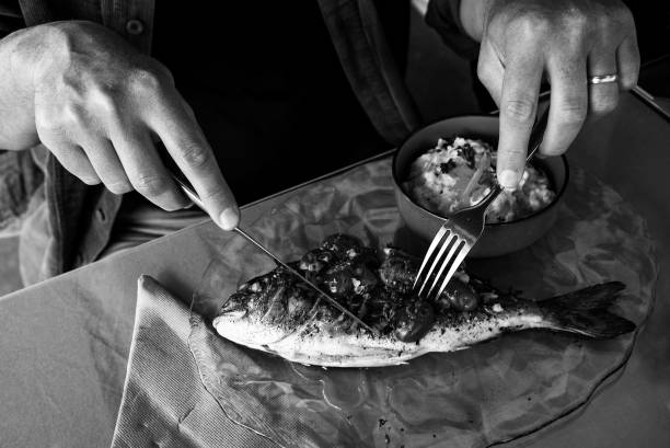 homme mangeant du poisson de daurade grillé et un risotto de légumes. photo noir blanc. - gourmet salad dinner prepared fish photos et images de collection