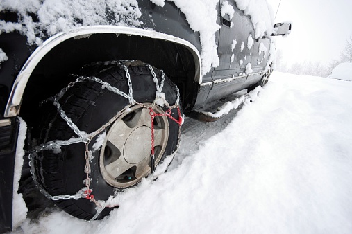 An SUV in the snow with chains on both front and rear tires.
