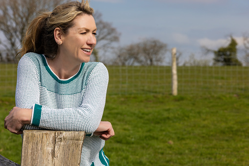Attractive smiling happy middle aged woman leaning resting on fence in the countryside