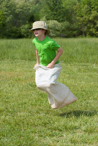 menino gunny corrida de saco, escola primária field day, pule alto - child playing sack race sports race - fotografias e filmes do acervo