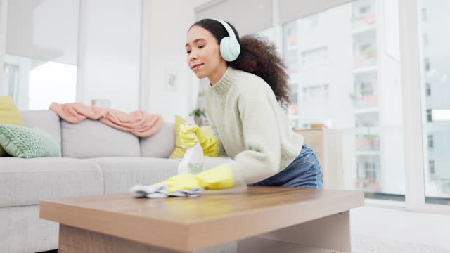 Headphone, spray and woman spring cleaning on a table in home living room as for hygiene, protection or disinfection. Dirt, dust and person or cleaner doing domestic or sanitary housekeeping work
