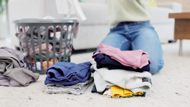 Hands, fold laundry and person with  pile of clean clothes in house on living room floor or housekeeper in spring cleaning. Washing, basket and order clothing by color or woman work in home service