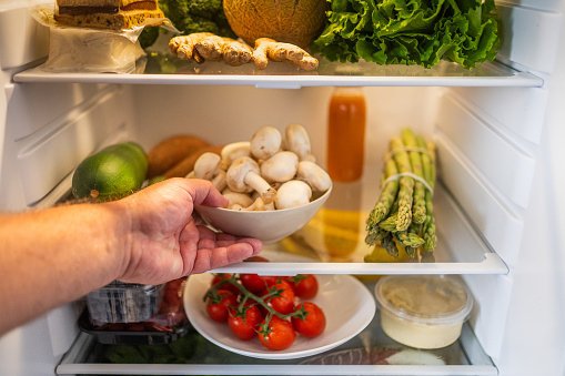 Close-up photo of a white person's hand grabbing a bowl of mushrooms from a refrigerator.