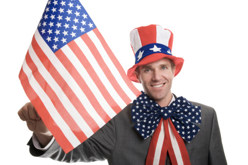 Guy in American flag hat and bow waves his American flag on white background
