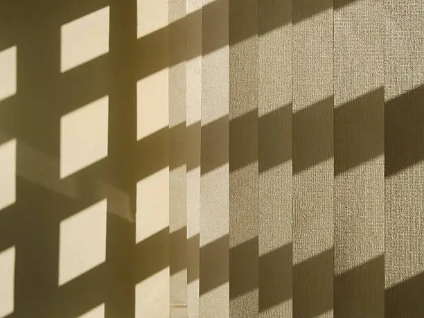 Pattern of light and shade on louvered window blinds (to the right) and the adjacent wall (to the left).