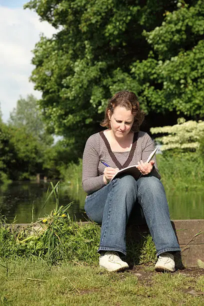 Photo of Young Woman sitting and writing in her Diary outdoors