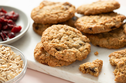 Closeup view of freshly baked oatmeal cranberry cookies on white marble board with oats and cranberries on a side