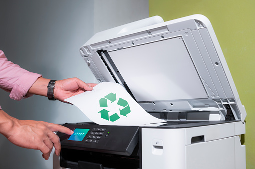 office worker prints paper on a multifunction laser printer with recycled paper in home office documents or paperwork. concept of World Environment Day and sustainable business.