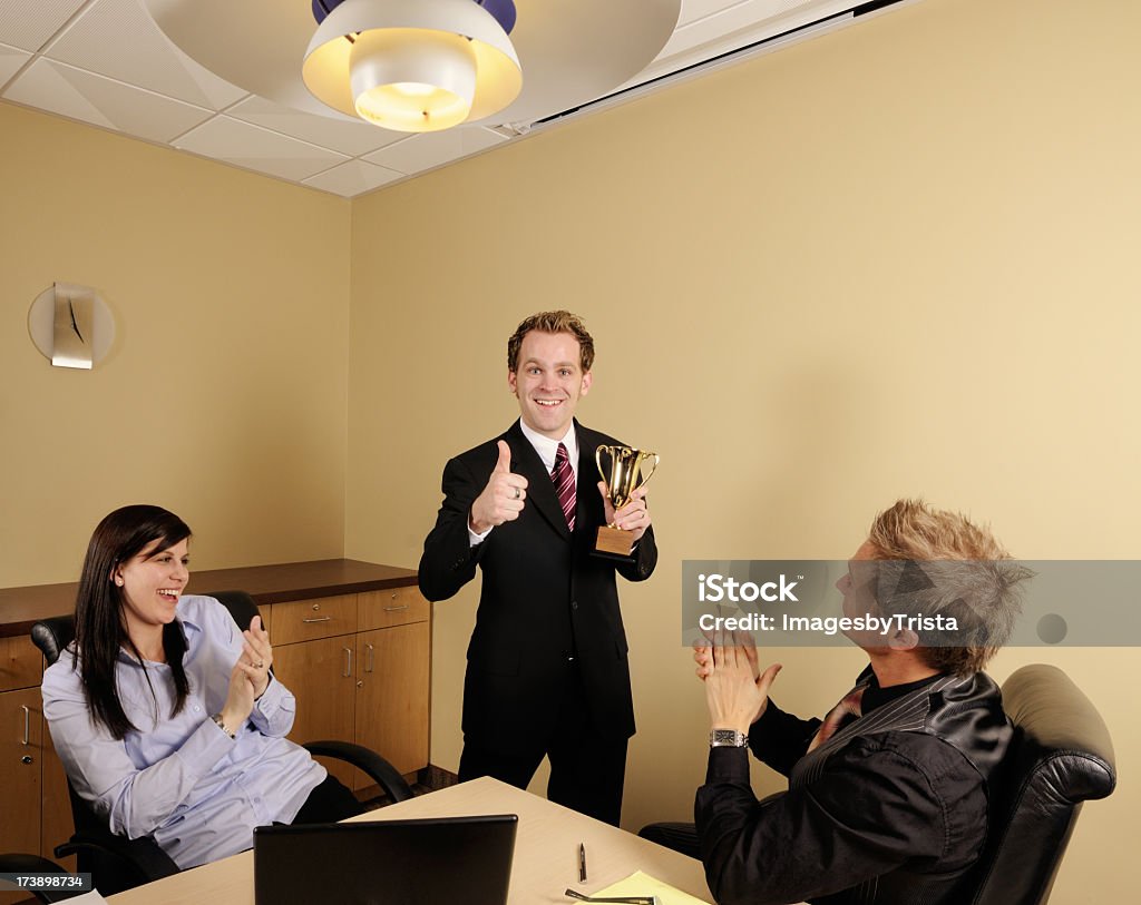 Positive Business Businessman giving the thumbs up sign while holding a trophy. 20-29 Years Stock Photo