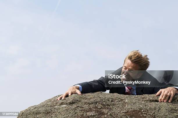 Trudności Biznesmen Clinging Do Krawędzi Windblown Rock - zdjęcia stockowe i więcej obrazów Humor