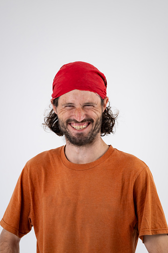 A young man with a beard and a red skull cap is looking at the camera and laughing