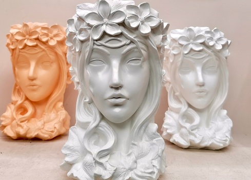 A plaster statuette in the form of a girl's face with a wreath on her head stands on a light shelf