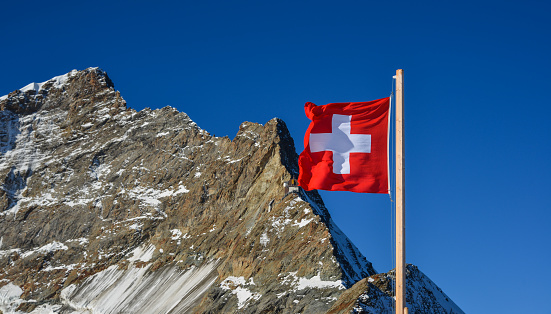 Swiss flag against top of Jungfrau (Switzerland), snow peak and blue sky background.