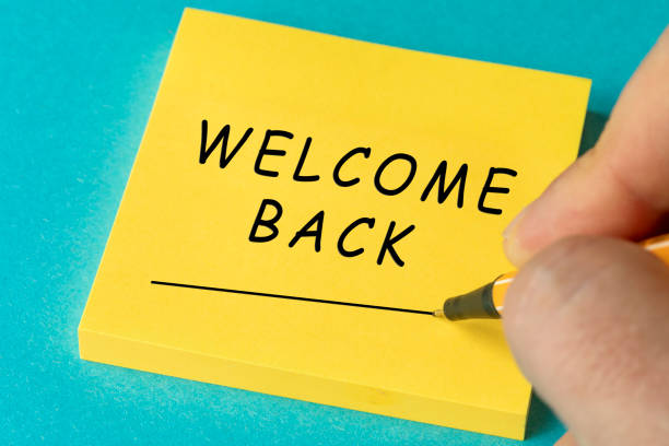 Paper notes with the words Welcome Back ON YELLOW STICKY PAPER NOTE AND BLUE BACKGROUND on a gray table, top view. Space for text