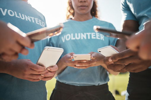 Volunteer, park and hands of people with phone for social media, online chat and charity website update. Community service, teamwork and men and women typing on smartphone outdoors for cleaning blog