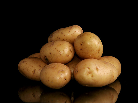 Moody black image of small baking potatoes, isolated on black with reflection.