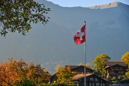 Swiss flag at the rural village with many traditional houses in autumn.
