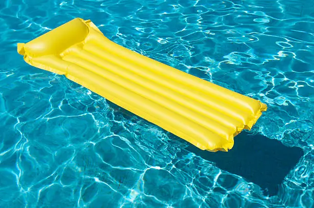 Bright yellow pool raft floats on the blue waters of an empty swimming pool